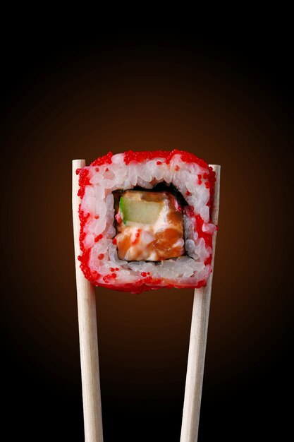 Sushi roll on chopsticks and black background
