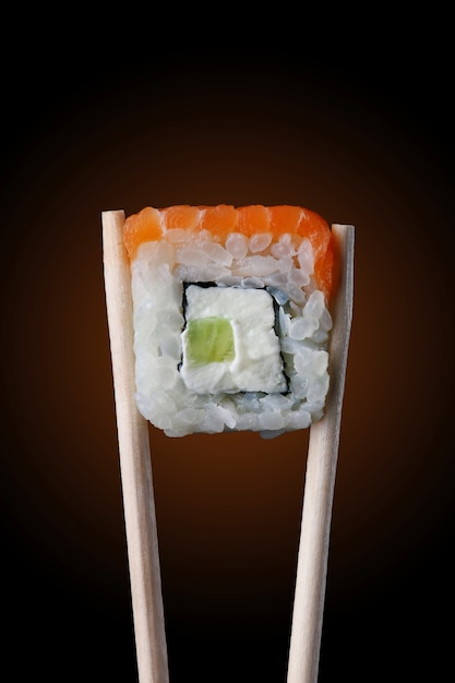 Sushi roll on chopsticks and black background