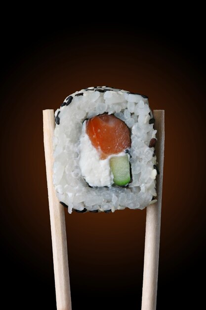 Sushi roll on chopsticks and black background