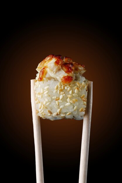 Sushi roll on chopsticks and black background