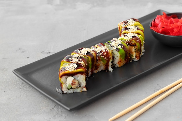 Sushi roll covered with avocado peels on black ceramic plate