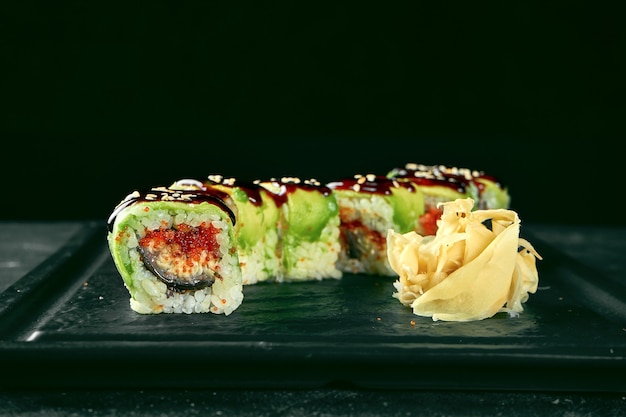 Sushi Roll groene draak met avocado, paling en tobiko kaviaar op een zwarte plaat op een donkere achtergrond. Voedsellevering. Japanse keuken