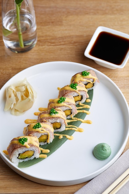 Sushi roll met spek op houten plaat met bloemen en sojasaus close-up. restaurant tafel concept