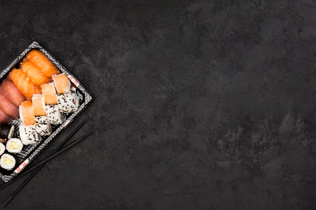 Photo sushi roll set on tray and chopsticks over dark textured surface with space for text