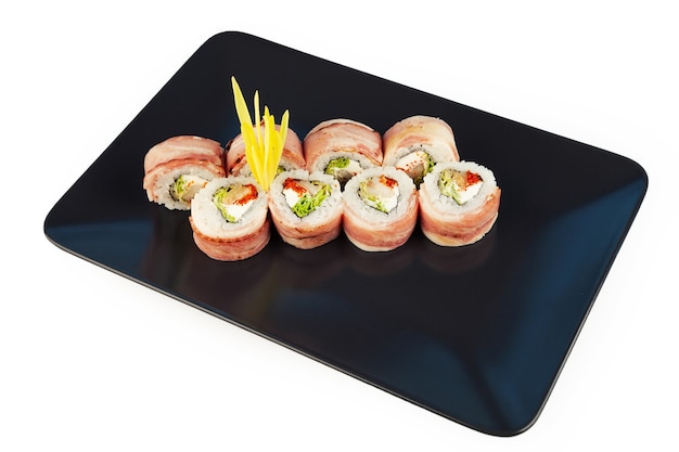 Sushi roll with bacon and fried sea bass on a black plate