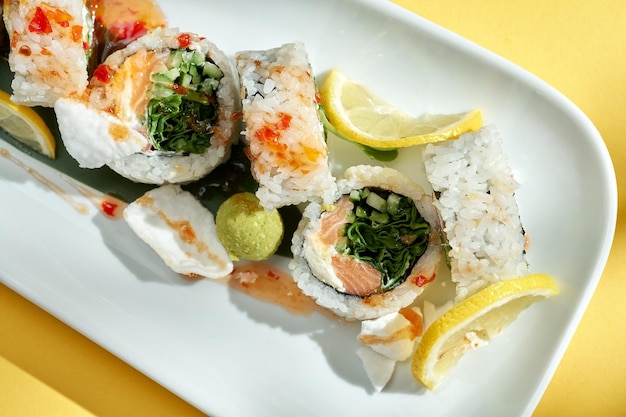 Sushi roll with cream cheese, cucumber and salmon in a white plate on a yellow background. hard shadows