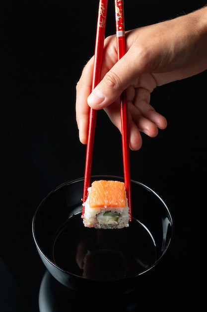 Sushi roll with reflection on a black background. A restaurant with Japanese cuisine. Women's hands holding sushi rolls