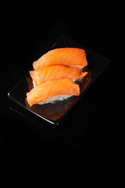 Sushi roll with reflection on a black background. A restaurant with Japanese cuisine. Women's hands holding sushi rolls