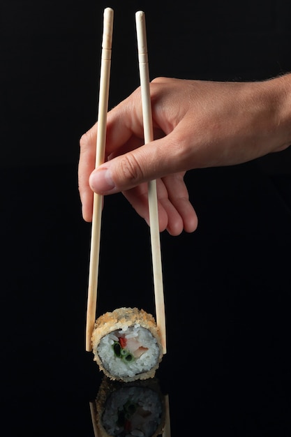 검정색 배경에 반사가 있는 스시 롤입니다. 일본 요리를 제공하는 레스토랑. 스시 롤을 들고 여성의 손