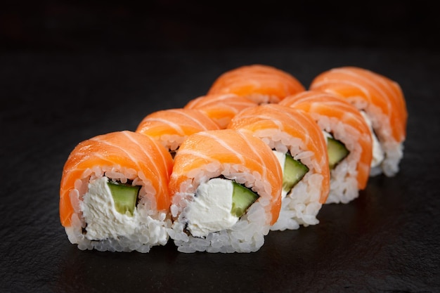 Sushi roll with salmon avocado and cream cheese on a black background