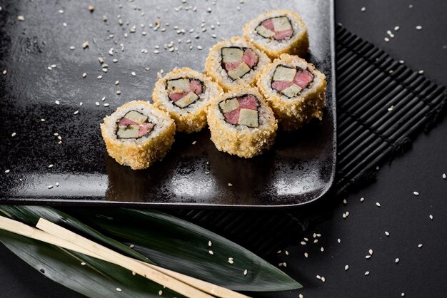 Sushi rolls on black plate with bamboo leaves and chopsticks