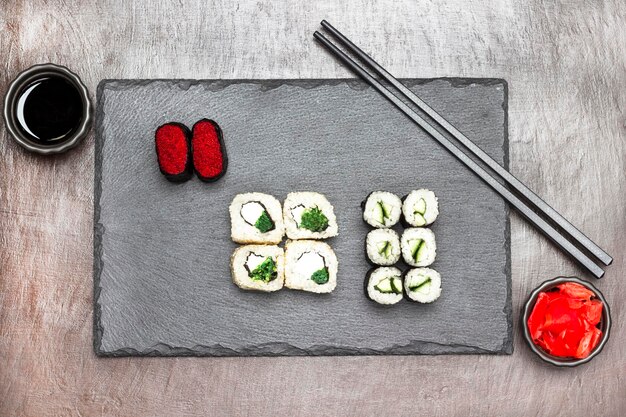Суши-роллы и палочки для еды на каменной доске Имбирь и соевый соус в мисках