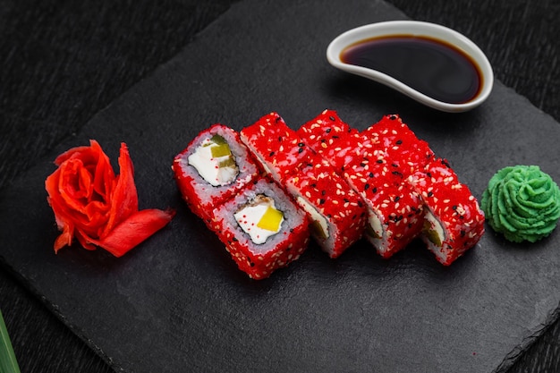 Sushi rolls laid out on a dark background decorated with bamboo leaves and chopsticks