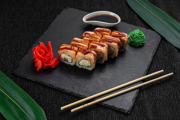 Роллы суши, выложенные на темном фоне, украшенные бамбуковыми листьями и палочками для еды
