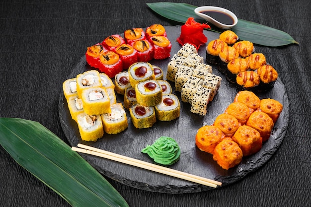 Sushi rolls laid out on a dark background decorated with bamboo leaves and chopsticks