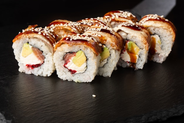 Sushi Rolls met zalm, avocado, paling, vliegende vis kaviaar en roomkaas binnen op zwart