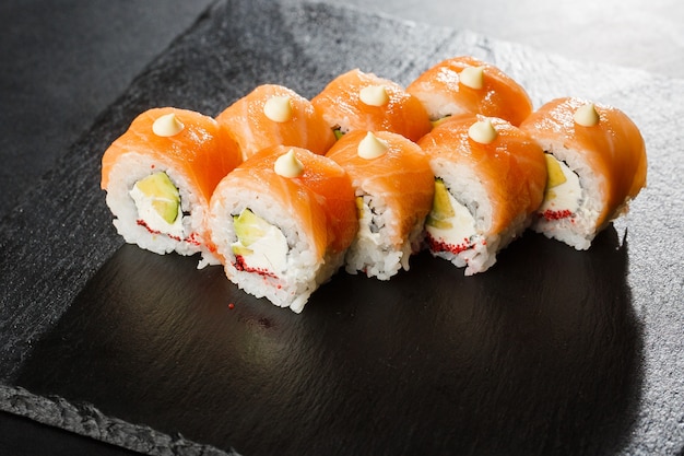 Sushi Rolls met zalm, avocado, vliegende vis kaviaar en roomkaas binnen op zwart