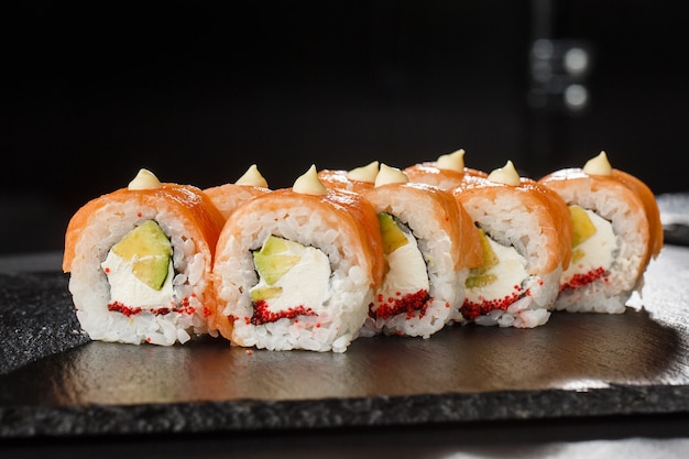 Sushi Rolls met zalm, avocado, vliegende vis kaviaar en roomkaas binnen op zwart