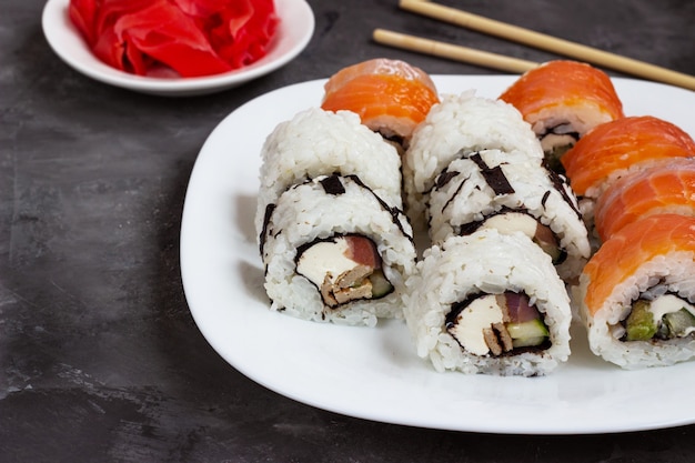 写真 黒いテーブルの上の白い皿に生姜のピクルスを添えて巻き寿司。