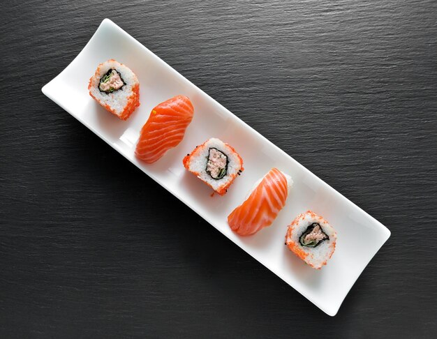 Sushi and rolls on a rectangular white plate and slate table