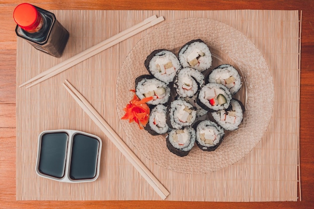 Sushi rolls on a round plate with sticks and soy sauce top view