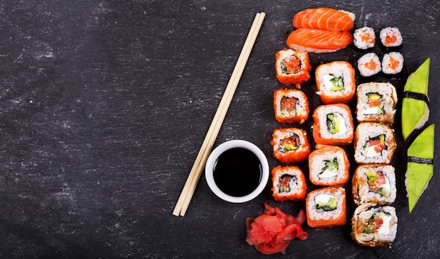 Sushi rolls set and sashimi on dark background, top view