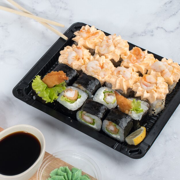 Sushi rolls set served on dark wooden board with wasabi, soy sauce and ginger.