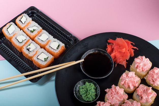 Sushi rolls set with red mayonnaise sauce and Philadelphia   served on black plate. Pink and blue table