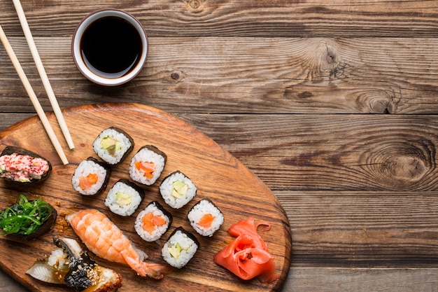 Sushi, rolls and spices on wooden light brown background