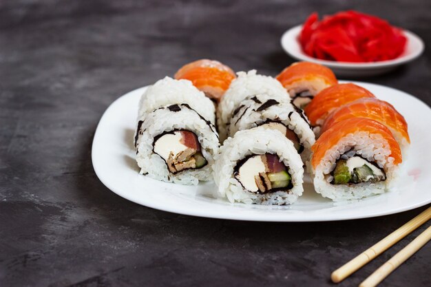 Sushi rotoli su un piatto bianco su un tavolo nero con zenzero sottaceto.