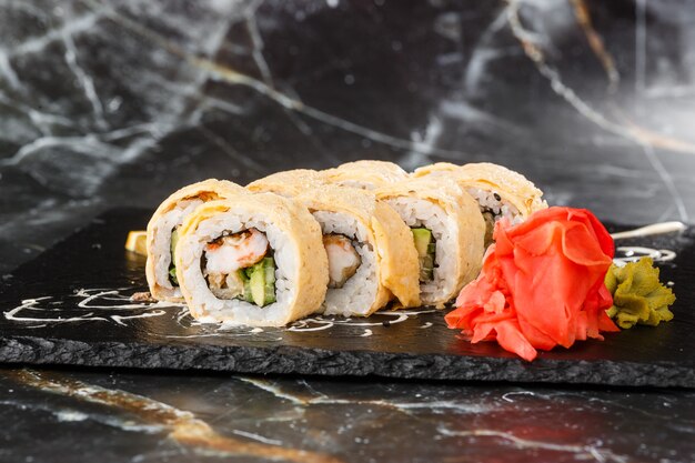 Sushi Rolls with avocado, eel, cucumber and cream cheese inside on black slate isolated on black marble background. California rolls covered on omelet Sushi menu. Horizontal photo.