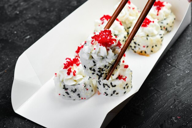 Суши-роллы с икрой, кунжутом и сыром Японская еда Доставка Одноразовая посуда На фоне черного камня