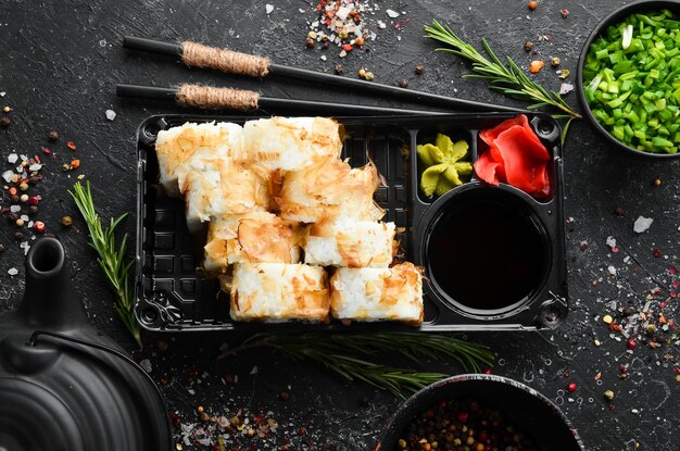 Photo sushi rolls with cheese and tuna chips wasabi and soy sauce in a plastic box top view