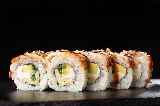 Sushi Rolls with cucumber, avocado, eel, omelet and Cream Cheese inside on black