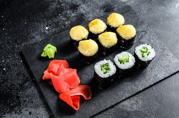 Sushi rolls with cucumber, salmon and shrimp on a stone tray. Black background. Top view