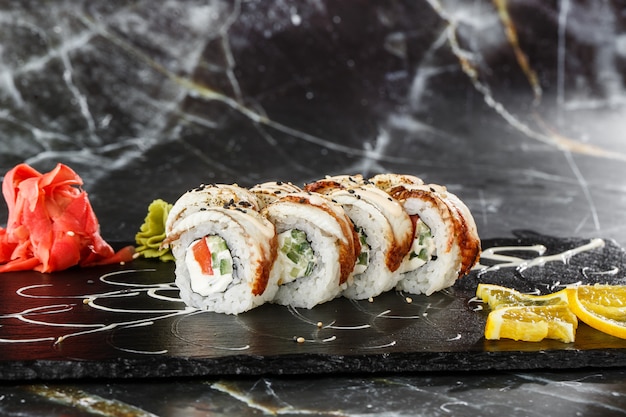 Sushi Rolls with cucumber, tomato, eel and Cream Cheese inside on black slate isolated on black marble background. Philadelphia unagi roll. Sushi menu. Horizontal photo.