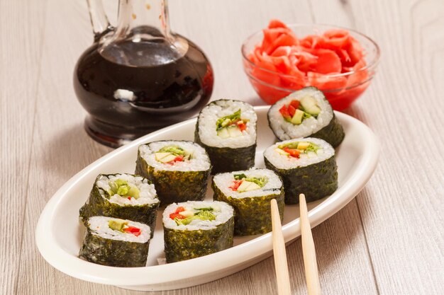 Sushi rolls with rice pieces of avocado cucumber red bell pepper and lettuce leaves on ceramic plate