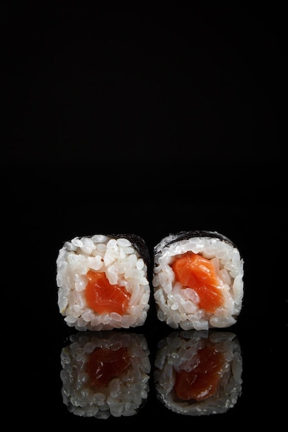反射と黒の背景にご飯とサーモンの巻き寿司