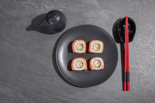 Sushi rolls with salmon avocado and cucumber on a black round plate on a black stone slate background