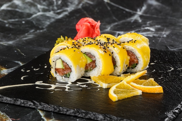 Sushi Rolls with salmon, avocado, omelet inside and mango on top. Sushi Rolls with salmon on black marble background. Sushi menu. Japanese food. Horizontal photo.