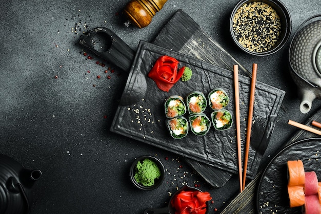 Фото Суши-роли с листьями лосося, капусты и сливочного сыра, подаваемые с соусом васаби и маринованным имбирем, японская традиционная еда.