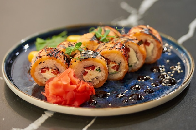 Sushi rolls with salmon Philadelphia cheese and tuna on a blue ceramic plate with sauce sesame  wasabi and leaves Black stone table