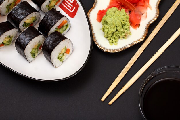 Sushi rolt in nori zeewiervellen met avocado en rode vis op keramische plaat. Bord met rode ingelegde gember en wasabi. Kom met sojasaus en houten stokken. Bovenaanzicht.