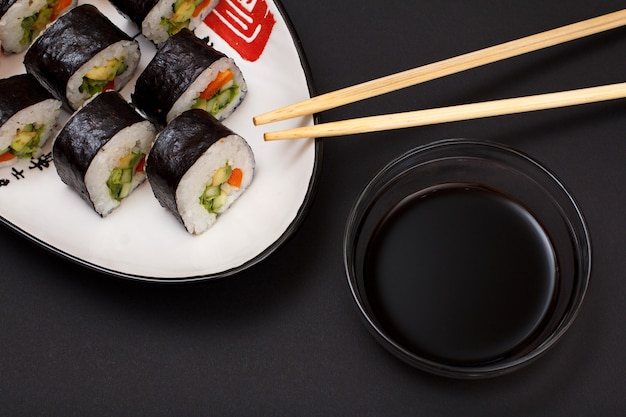 Sushi rolt in nori zeewiervellen met avocado en rode vis op keramische plaat. Kom met sojasaus en houten stokken. Bovenaanzicht met zwarte achtergrond.