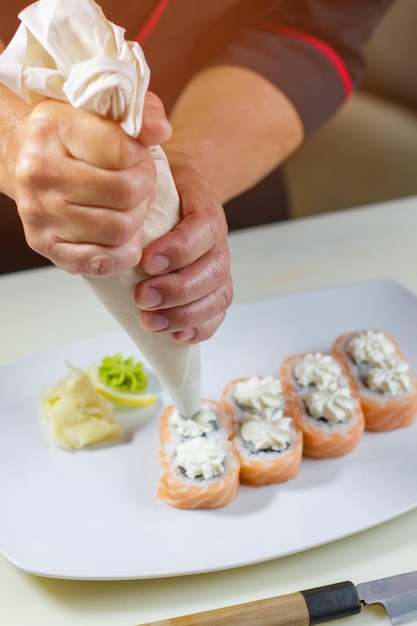 Sushi rolt op plaat. Spuitzak in iemands handen. Japans gerecht met roomkaas. Smakelijke uramaki-broodjes.