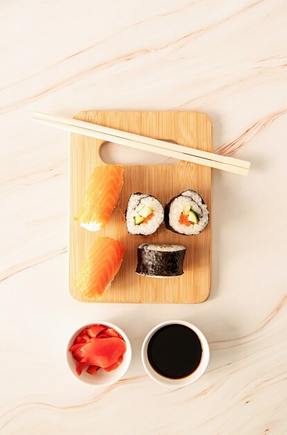 Sushi salmon set on wooden cutting board. Asian food on beige marble background top view