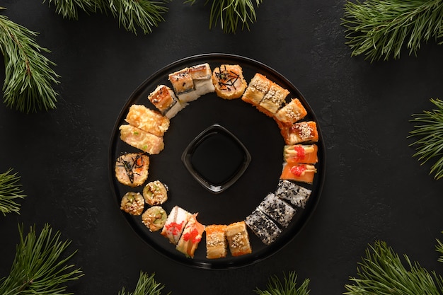 Sushi set as Christmas wreath decorated fir tree branches on black background. View from above. Copy space. Delivery food.