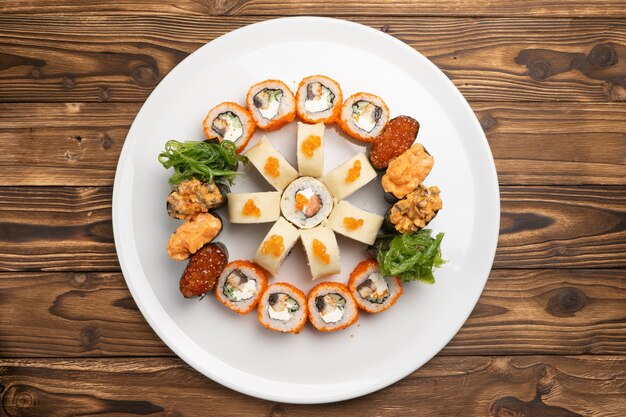 Sushi set of maki rolls with salmon and eel and gunkans with caviar and chuka salad on a white round ceramic plate