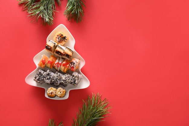 Foto sushi impostato nella piastra come albero di natale decorato rami di abete su sfondo rosso. vista dall'alto. spazio per il testo. stile flatlay.