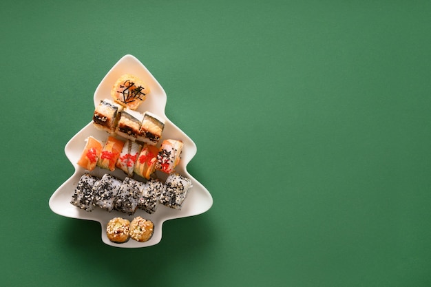 Sushi set in plate as Christmas tree decorated on green background. View from above. Space for text. Flatlay style.